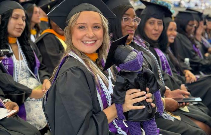 smiling grad at Commencement holding a crocheted mascot